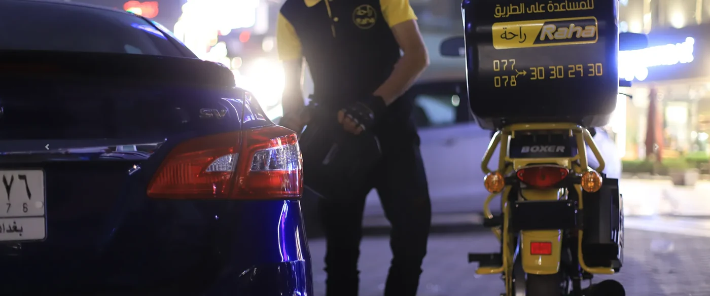 أحد أفراد فريق راحة يقدم خدمة توصيل الوقود إلى سيارة متوقفة ليلًا